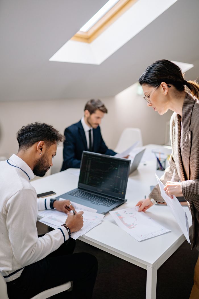 Three coworkers collaborate around a laptop in a bright, modern office setting.